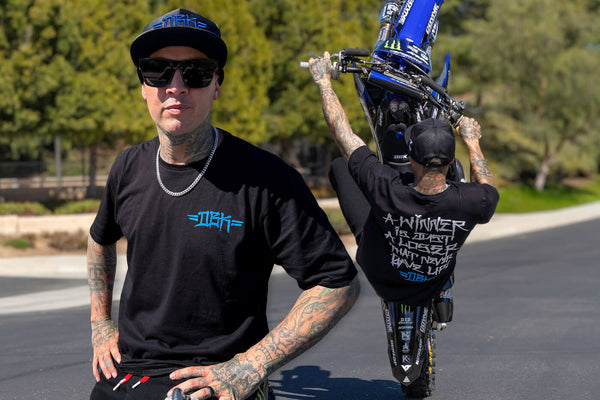 Jeremy Twitch Stenberg doing a motorcycle wheelie, wearing a black DBK shirt and black hat
