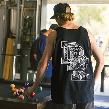 Black adult tank top back view with oversized detailed bandana-style DBK graphic, worn by man at a pool table in a garage lifestyle setting

